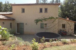 A two-story building with a tiled roof, a trampoline in the yard, and a bicycle parked outside.