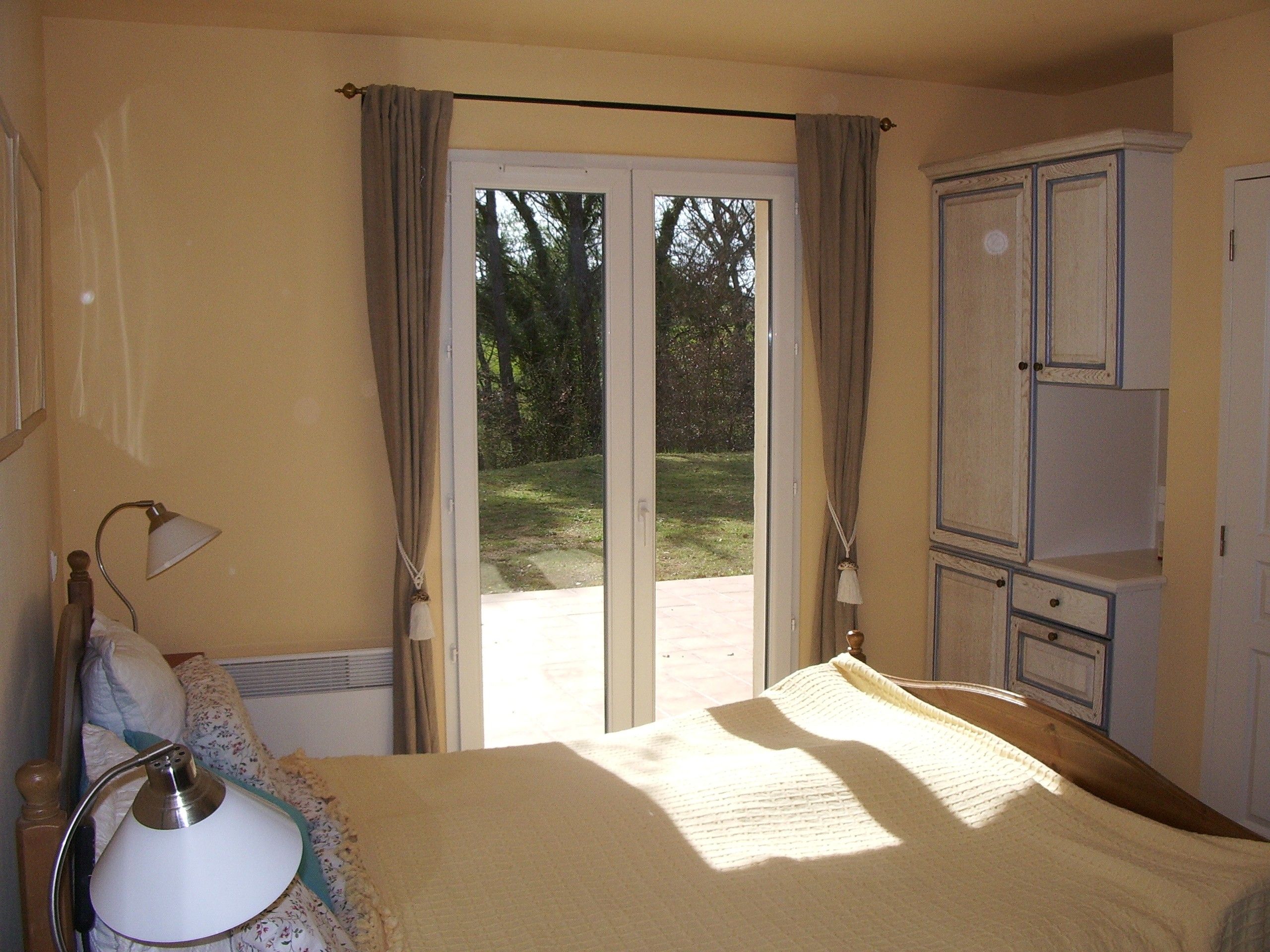 Una camera da letto con un letto, un comodino, una lampada, un armadio e una porta scorrevole in vetro che dà su un giardino.
