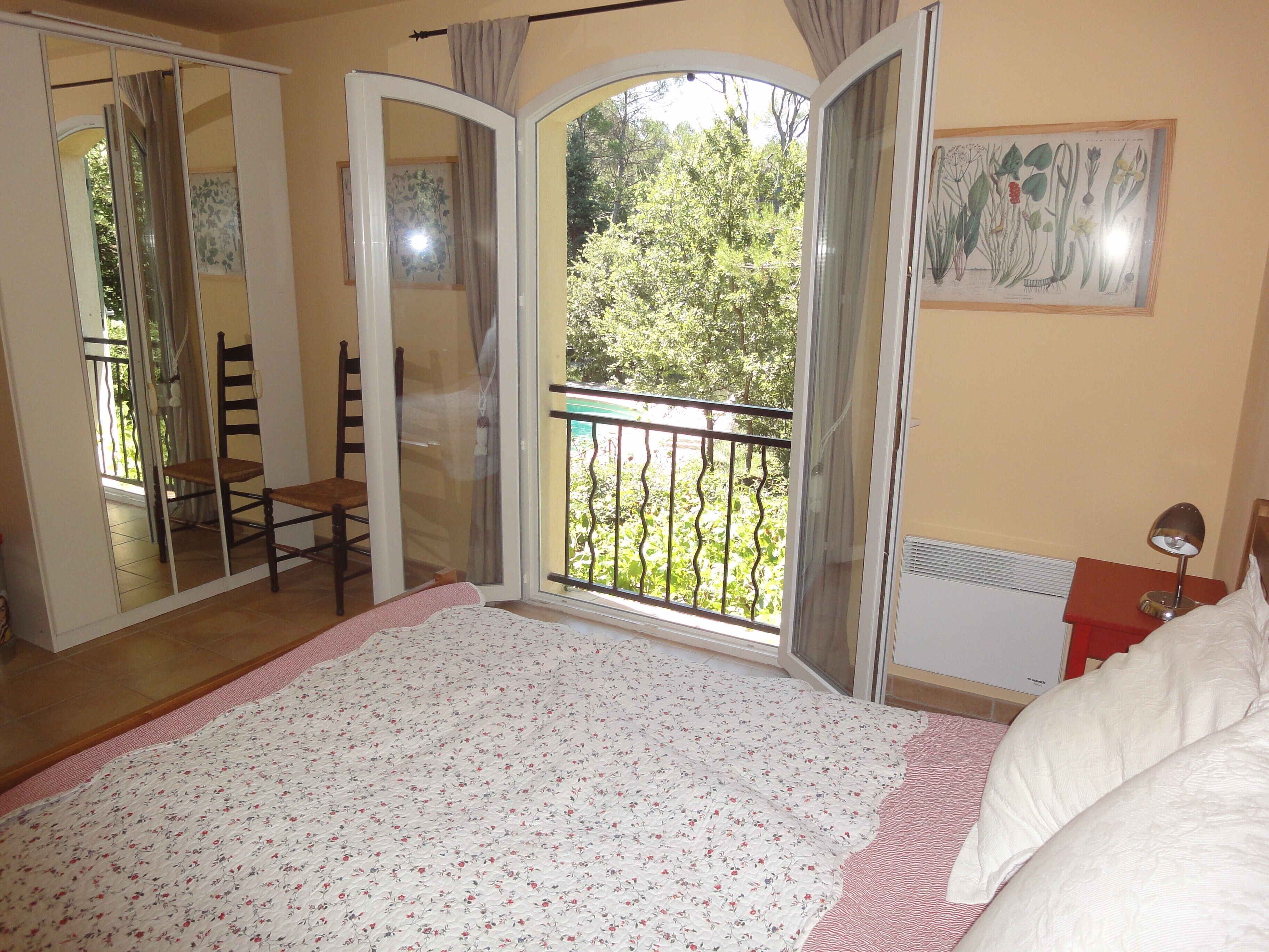 Un dormitorio con una cama grande, un balcón con vistas a árboles y un cuadro en la pared.