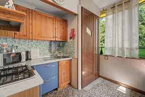 A compact kitchen with wooden cabinets, a microwave, a stove, and a window with curtains. - Apartment 'Camera Giuly' with Shared Garden, Wi-Fi and Air Conditioning (Venice)