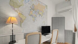 Una habitación con un gran mapa mundial en la pared, un escritorio con una computadora, dos sillas, una lámpara y un equipo de aire acondicionado.
