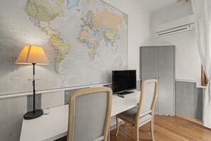 Ein Zimmer mit einer großen Weltkarte an der Wand, einem Schreibtisch mit Computer, zwei Stühlen, einer Lampe und einer Klimaanlage.