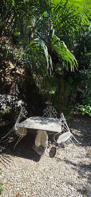A metal bench with intricate designs, situated on a gravel surface, surrounded by dense foliage. - Gaia Room with Shared Garden, Wi-Fi and Air Conditioning (Venice)