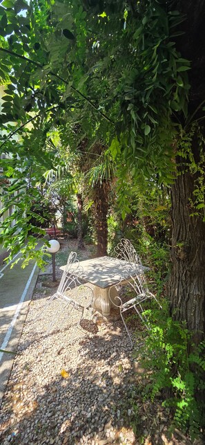 Ein Gartenbereich mit einer Steinsitzbank, umgeben von Kies, einem Metallzaun und üppiger Bepflanzung.