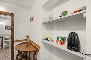 A kitchen with a wooden table, a shelf with kitchen items, and a wall-mounted coffee machine. - 'Camera Petit' Apartment with Shared Garden, Wi-Fi and Air Conditioning (Venice)
