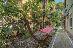 A hammock in a garden area with a paved walkway and a building in the background. - 'Camera Petit' Apartment with Shared Garden, Wi-Fi and Air Conditioning (Venice)
