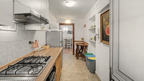Une cuisine étroite avec une cuisinière à gaz, des placards blancs et une table en bois.