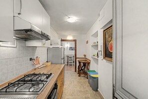 A narrow kitchen with a gas stove, white cabinets, and a wooden table. - 'Camera Rose' Apartment with Shared Garden, Wi-Fi, and Air Conditioning (Venice)