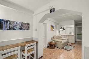 A hallway with a wooden bench, a beige armchair, and a small table with a lamp. There are two framed pictures on the walls. - 'Camera Rose' Apartment with Shared Garden, Wi-Fi, and Air Conditioning (Venice)
