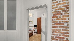 Un couloir menant à une chambre avec un mur en briques, un lit, un bureau et un téléviseur.