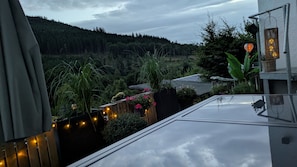 A residential area with a view of a forested hill, a wooden deck with string lights, and a house with a sloped roof.