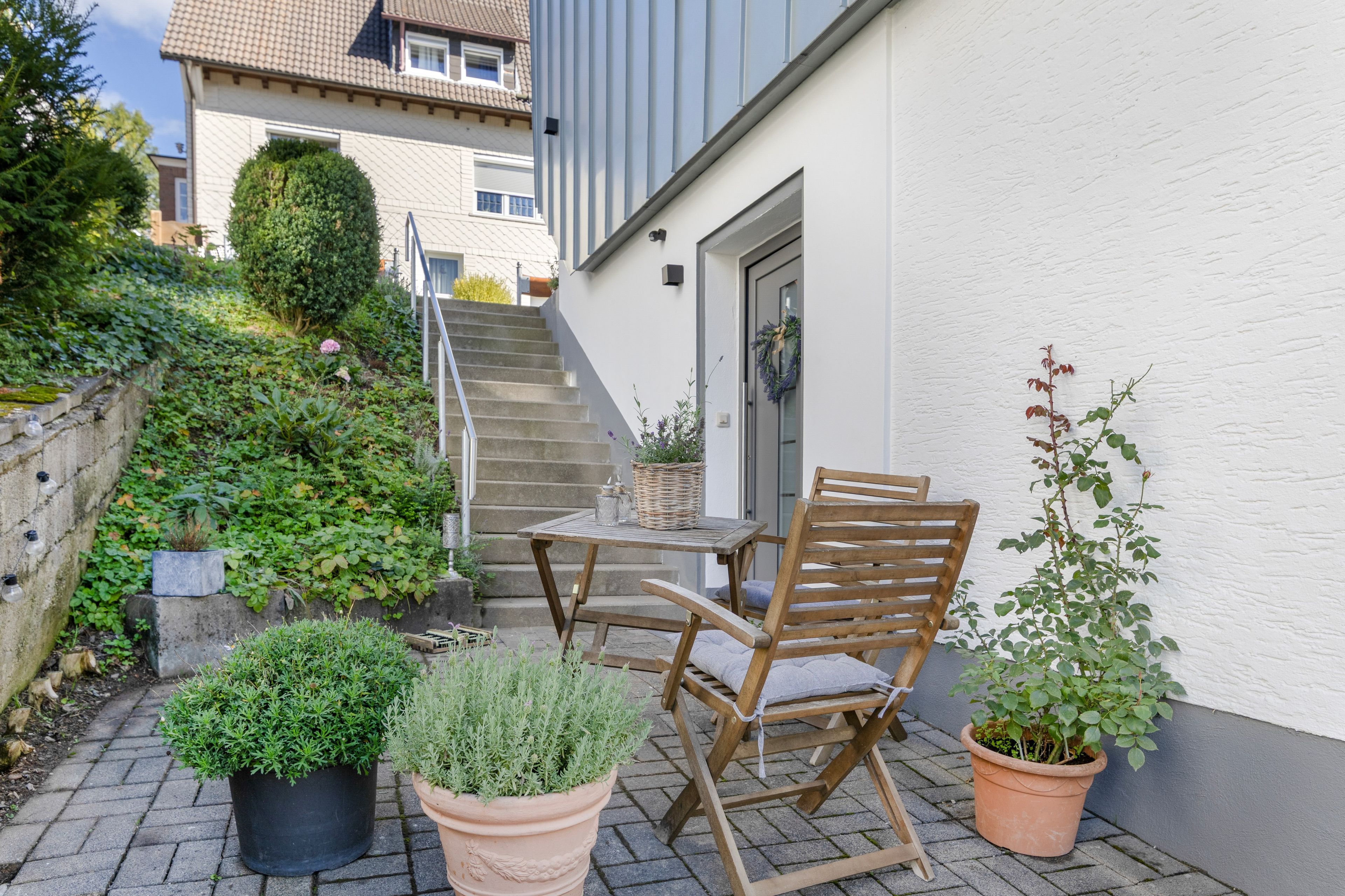 A patio with a table and chairs, potted plants, and a staircase leading to a building.