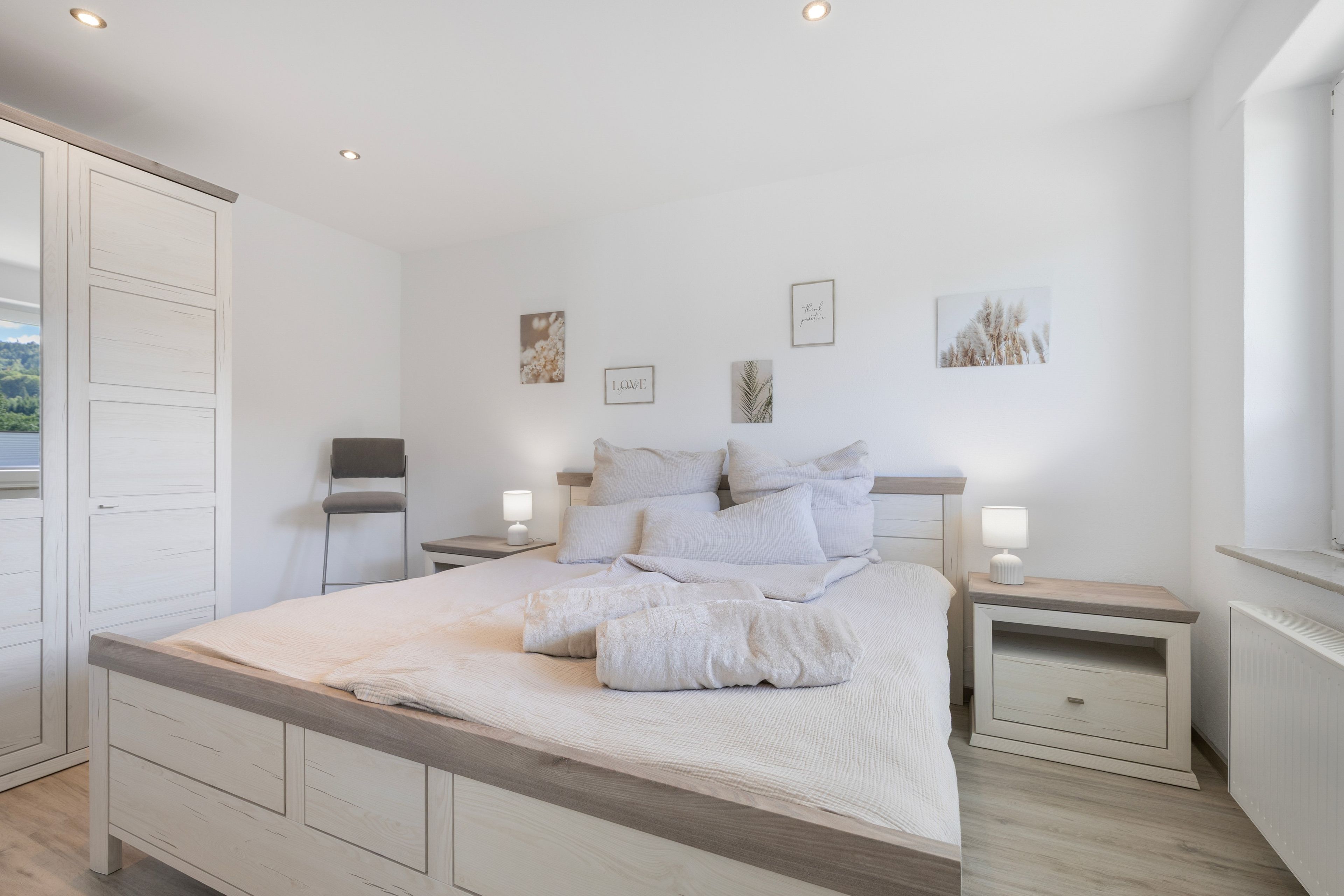 A bedroom with a large bed, two bedside tables, a wardrobe, and wall art.