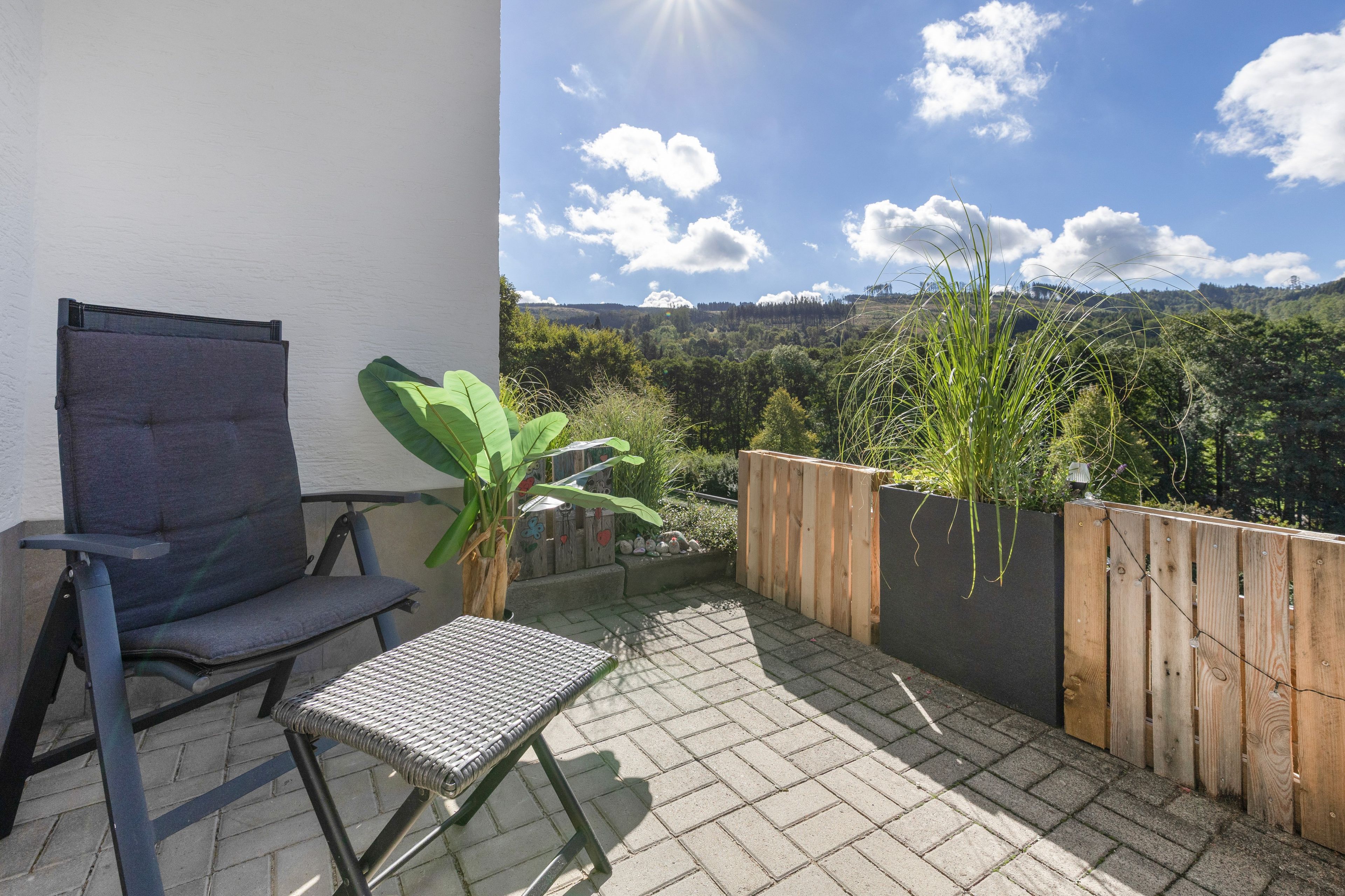 Ein Balkon mit Stuhl, kleinem Tisch und einer Holzlattenveranda mit Pflanzen.