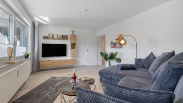 A modern living room with a flat-screen TV, a bookshelf, a sofa, and a dining area with a table and chairs.
