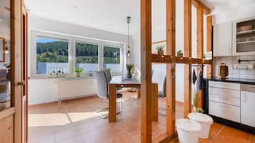 A modern kitchen with wooden beams, a dining area with a view of the forest, and a window with blinds.
