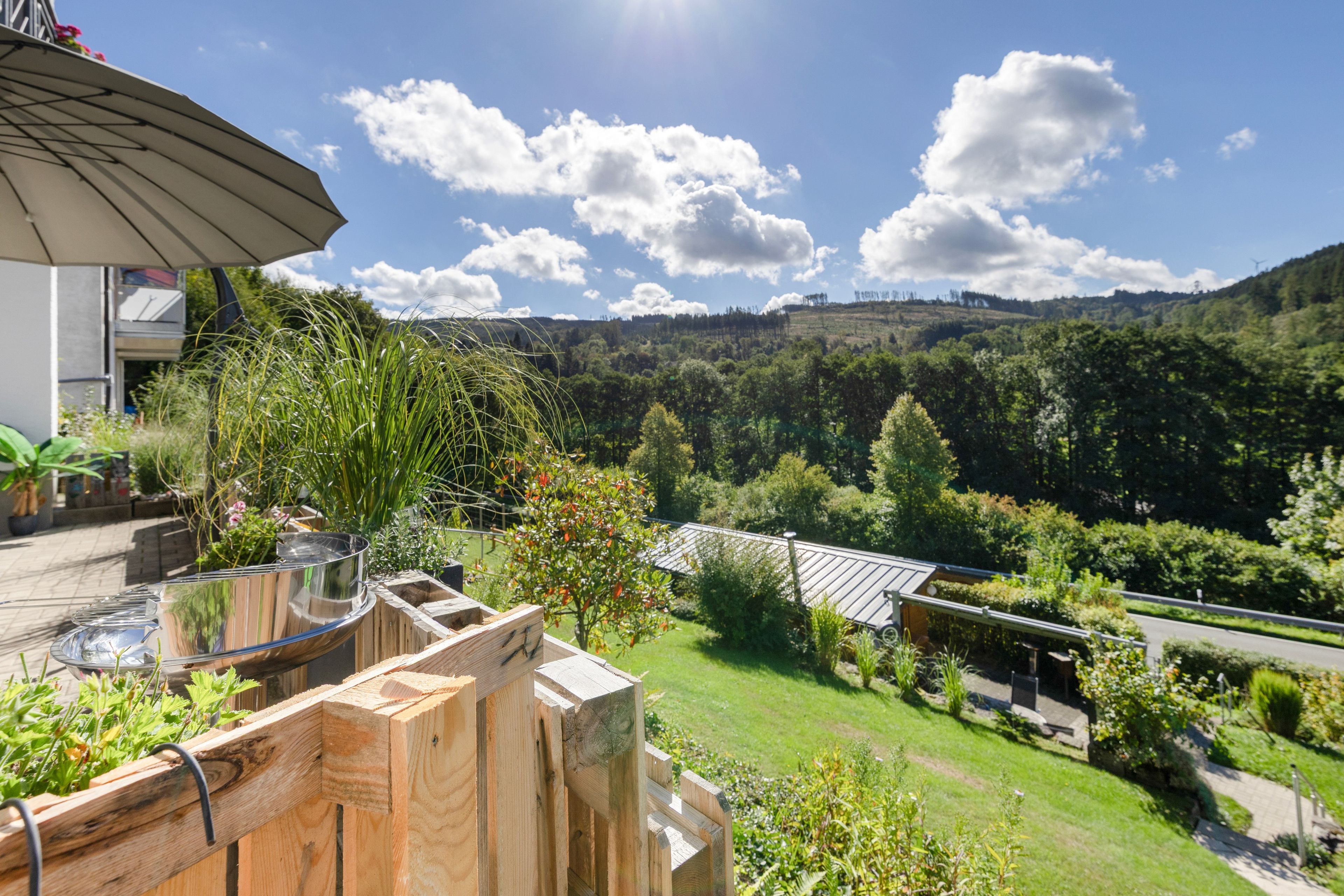A patio with a glass-top table, wooden deck, and a view of a green landscape with trees and hills.