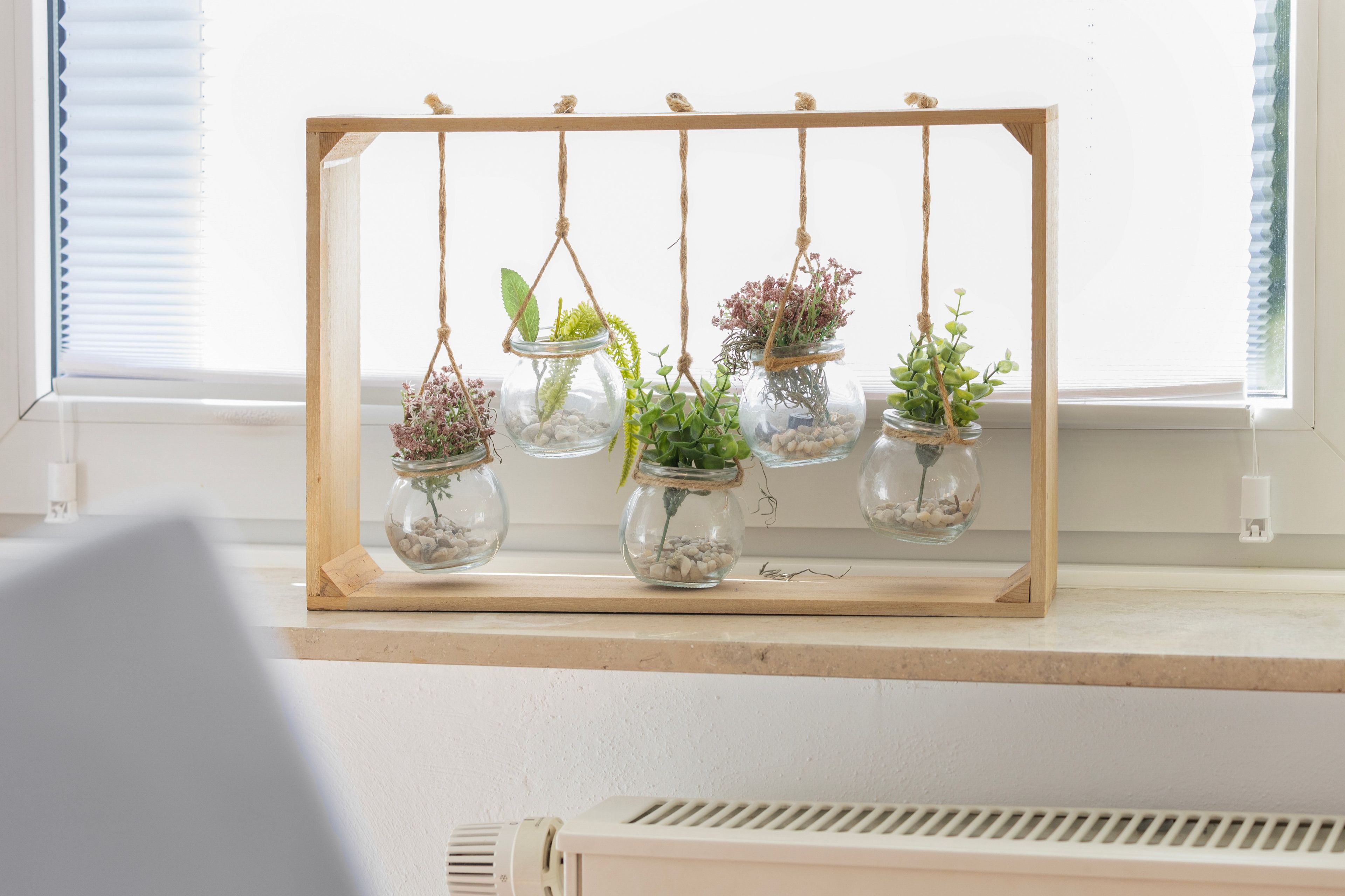 Une étagère en bois avec des bocaux en verre suspendus contenant des plantes.