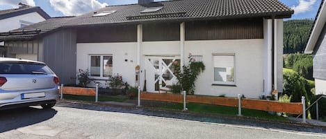 Ein zweistöckiges Haus mit weißer Fassade, einem Ziegeldach und einem Holzzaun.
