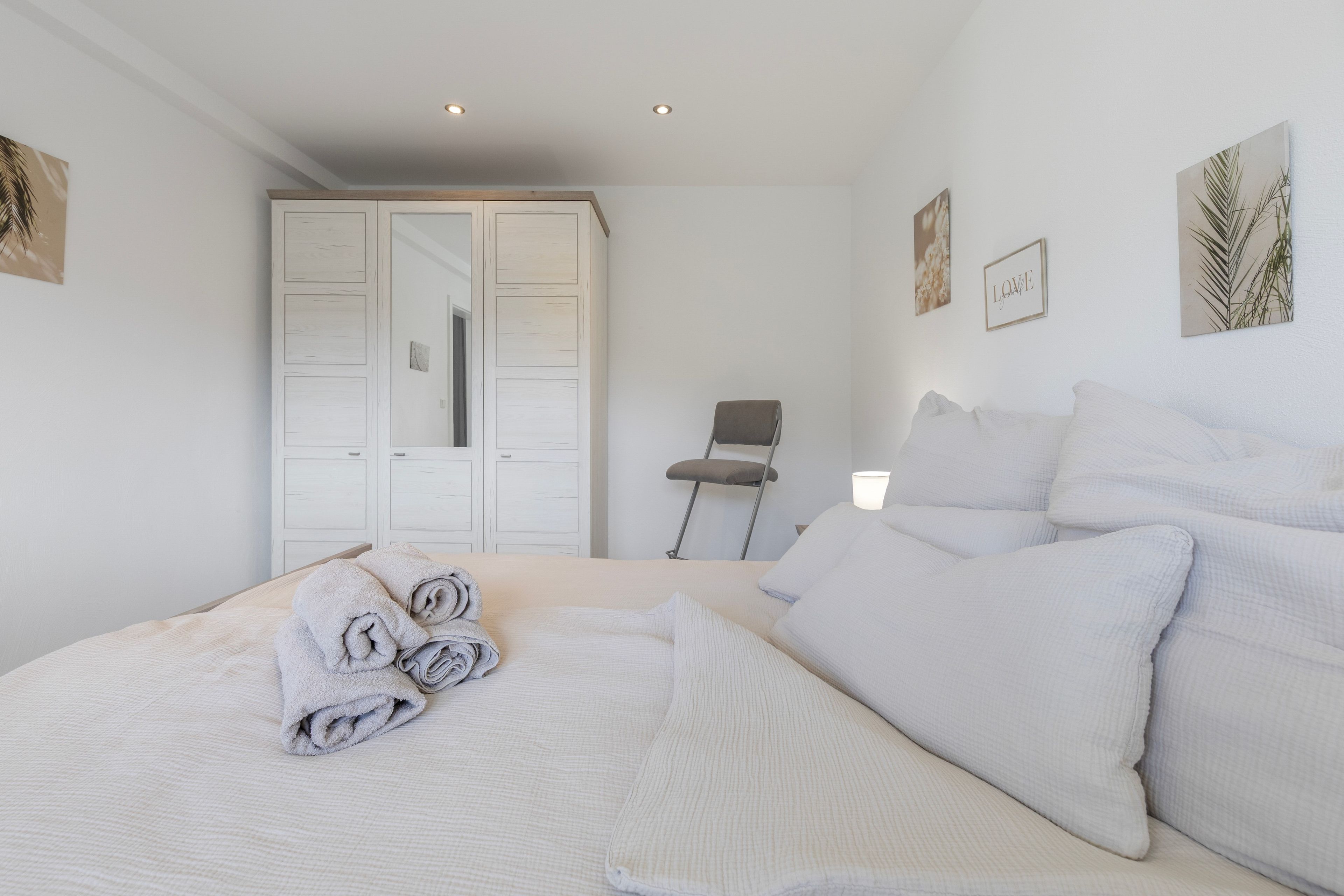 Une chambre à coucher avec un lit, des oreillers, une chaise, une armoire et des œuvres d’art murales.