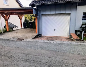 A garage with a white door, a wooden bench, and a covered area with a metal roof.