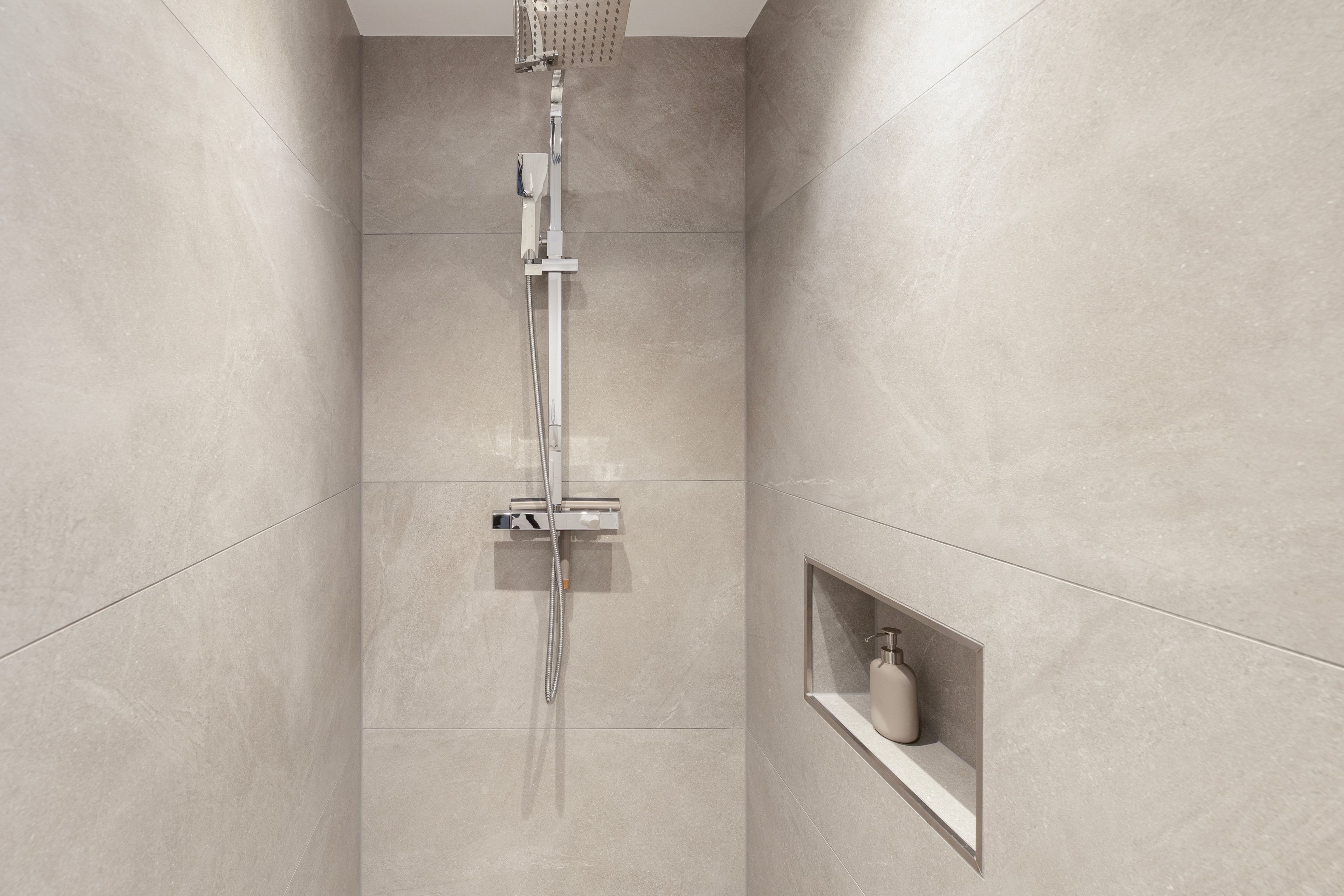 A modern shower with a handheld showerhead and a wall-mounted control panel.