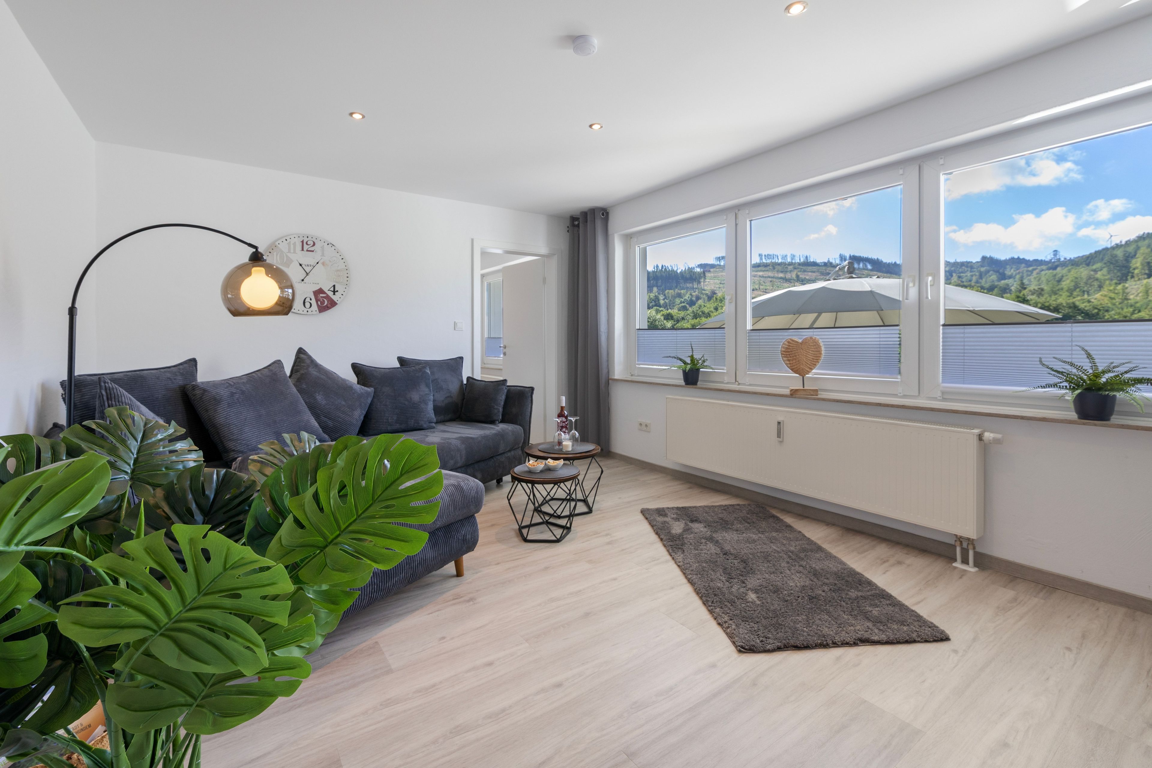 A modern living room with a sofa, a coffee table, and a view of a lake through large windows.