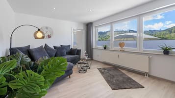 A modern living room with a sofa, a coffee table, and a view of a lake through large windows.