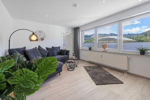 Un salon moderne avec un canapé, une table basse et une vue sur un lac, visible à travers de grandes fenêtres.