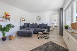 A modern living room with a grey sofa, a side table, a lamp, and a large window. - Apartment 'Bei Walli' with Private Terrace and Wi-Fi (Kirchhundem)