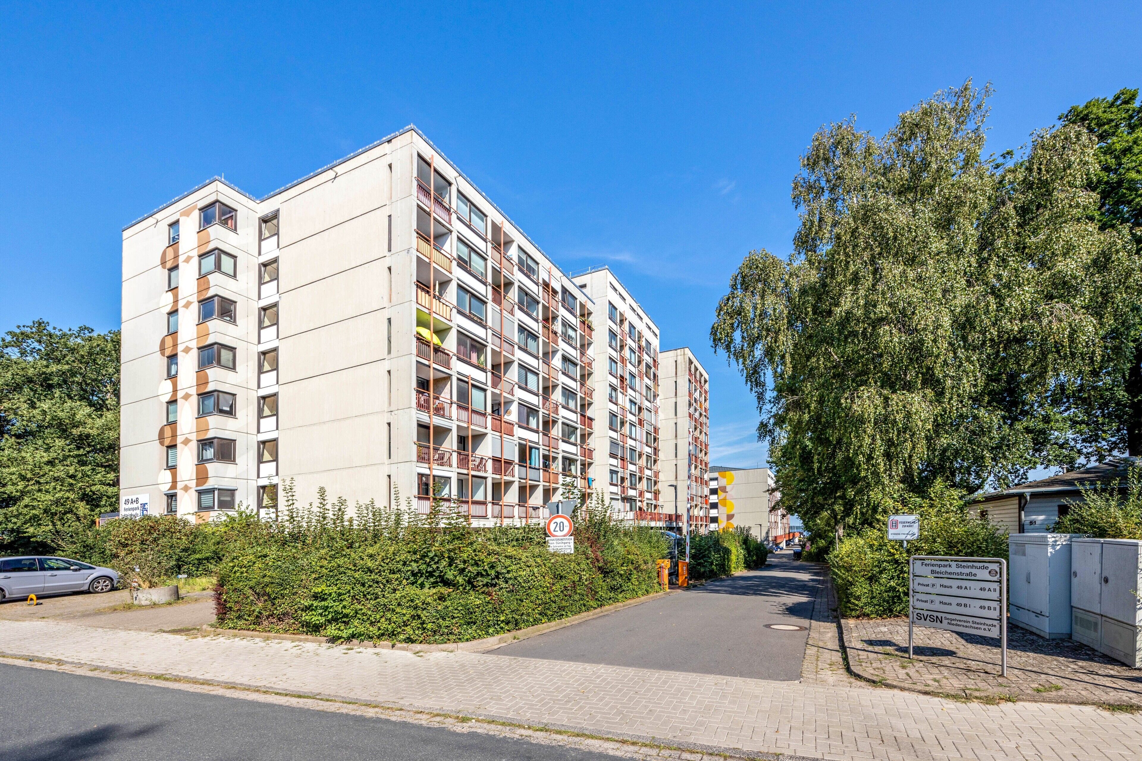 Un immeuble résidentiel à plusieurs étages, doté de balcons, avec une route pavée devant et un ciel dégagé.