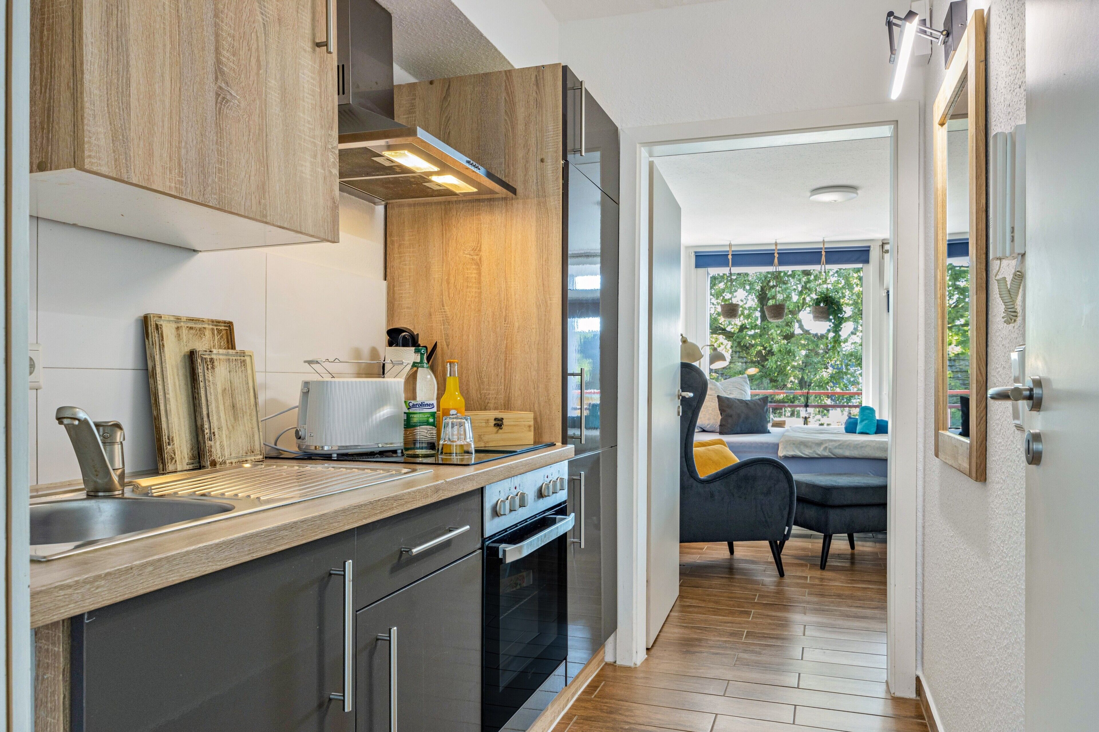 Een moderne keuken met roestvrijstalen apparatuur, houten keukenkastjes en uitzicht op een woonruimte met een bank en raam.