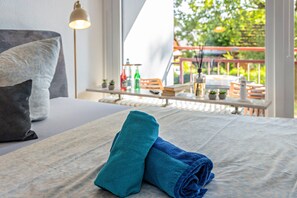 Ein ordentlich bezogenes Bett mit einem zusammengerollten Handtuch, einem Kissen und einer Lampe im Hintergrund.