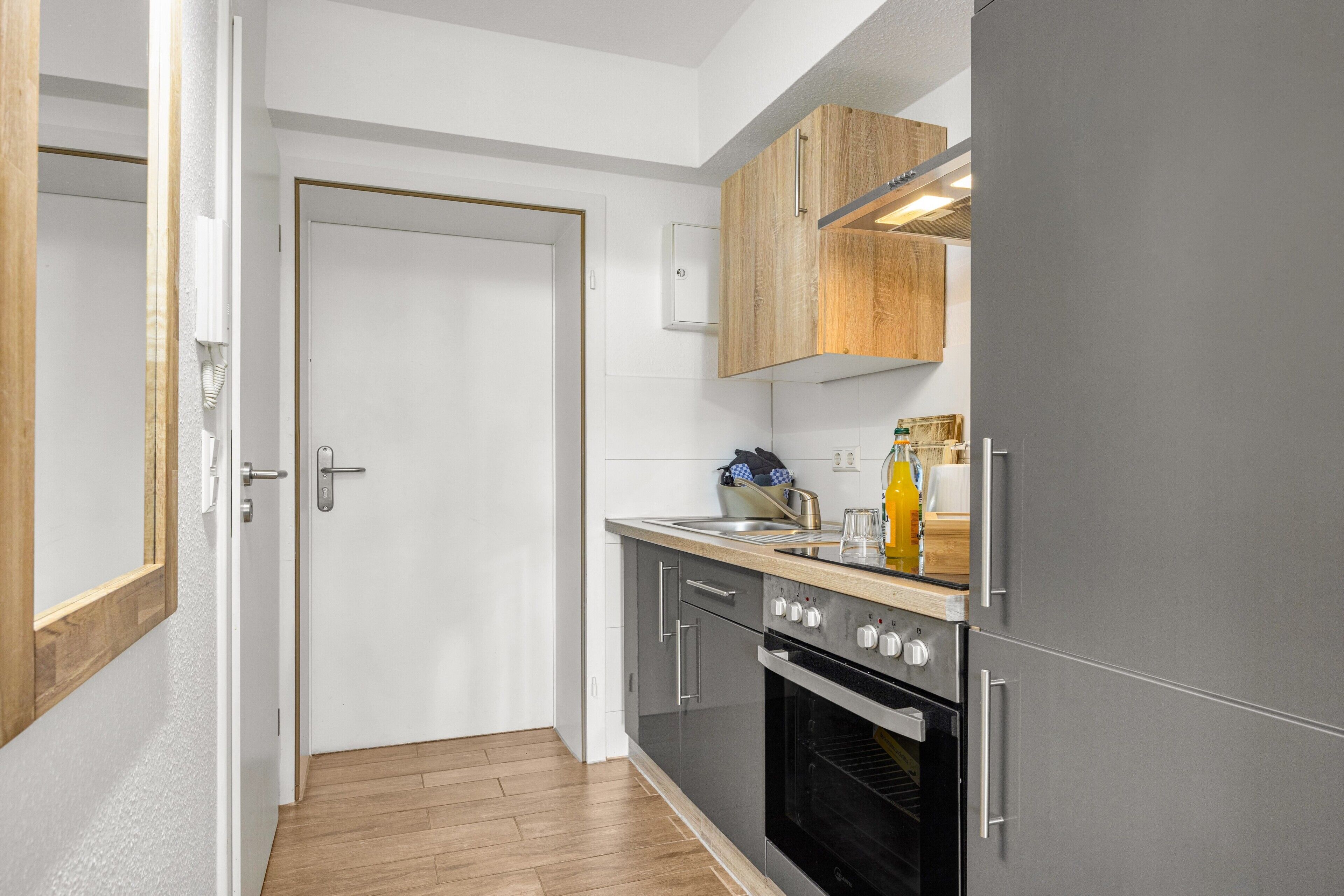 A modern kitchen with a built-in oven, a stainless steel sink, and wooden cabinets.