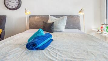 A neatly made bed with a patterned bedspread, two pillows, and rolled towels on a headboard.