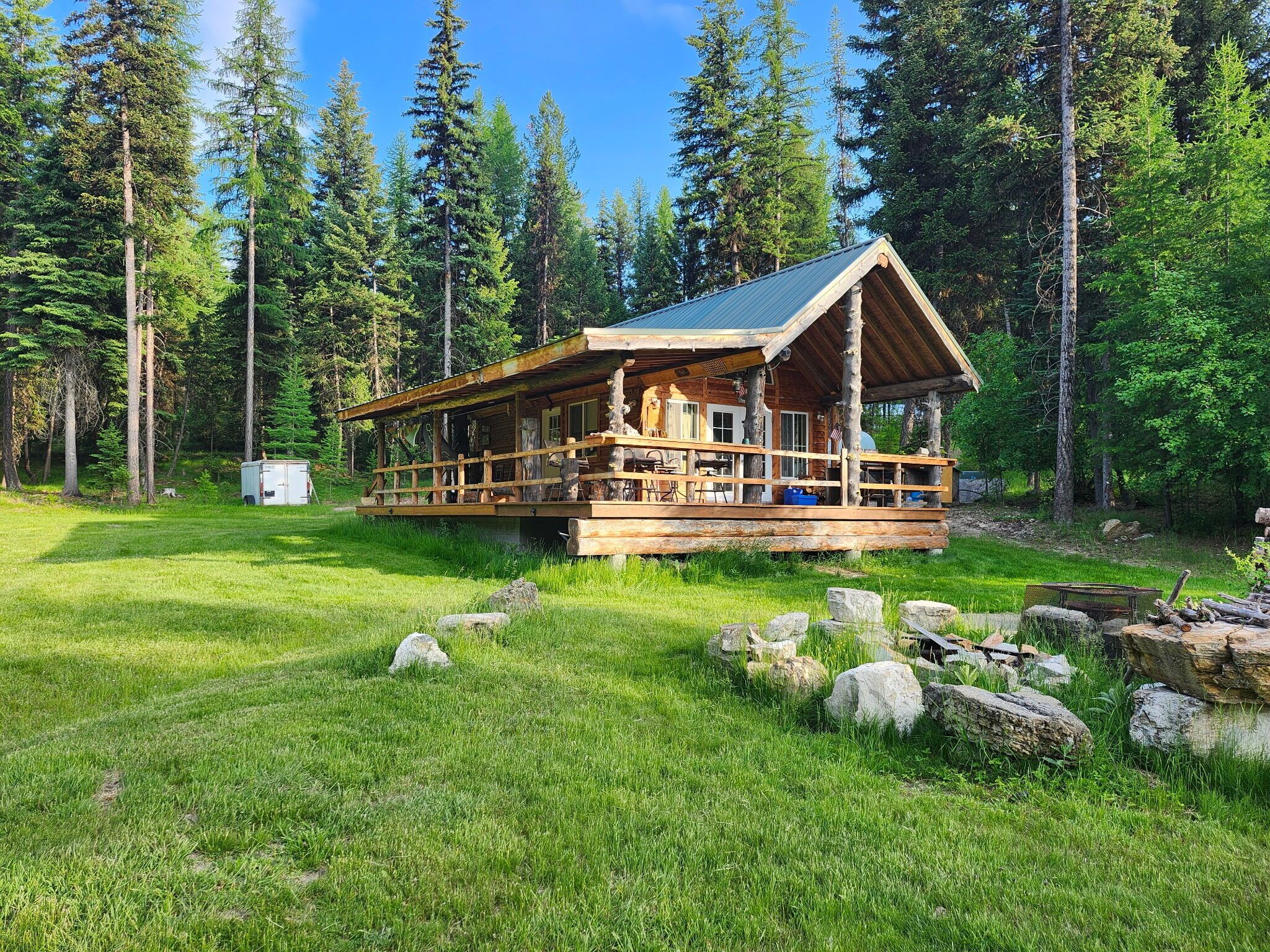 Eine rustikale Holzhütte mit einer Holzterrasse und einem Metalldach, umgeben von einem Wald.