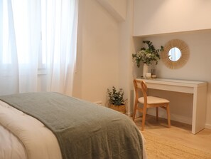 A bedroom with a bed, a desk, a chair, a potted plant, and a mirror.