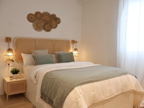 Een slaapkamer met een rotan hoofdbord, twee bedlampen, een groene plaid en een decoratief wandobject.