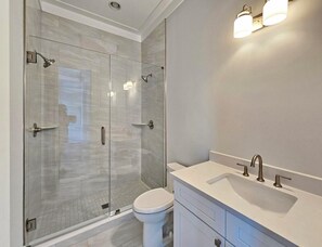 Ein modernes Badezimmer mit einer gläsernen Duschkabine, einer weißen Toilette und einem Waschtisch inklusive Spüle und Spiegel.