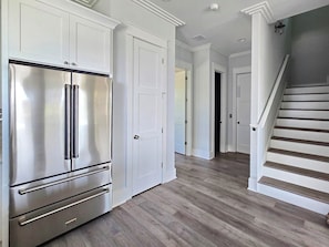 A kitchen with a stainless steel refrigerator, white cabinetry, and a wooden staircase. - Vista Del Mar: New Construction, Beach Views, Private Pool, Pet-Friendly, SGI Pl (St. George Island)