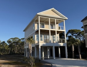 A two-story building with a balcony on the upper floor, surrounded by trees. - Vista Del Mar: New Construction, Beach Views, Private Pool, Pet-Friendly, SGI Pl (St. George Island)