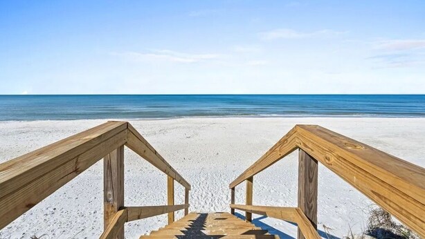 Una scala di legno conduce a una spiaggia sotto un cielo azzurro e limpido.