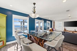 A modern dining area with a glass table and chairs, a ceiling light fixture, and a large window with a view. - Aloha House – Gulf-Front Retreat on Cape San Blas (Cape San Blas)