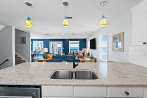 A modern kitchen with a marble countertop, stainless steel sink, and overhead pendant lights. - Aloha House – Gulf-Front Retreat on Cape San Blas (Cape San Blas)