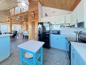 A modern kitchen with a refrigerator, microwave, and stove. There is a dining area with a table and chairs. - The Lookout: North Cape, 3 Bedrooms, Pet-Friendly, Private Pool! Short walk to b (Cape San Blas)
