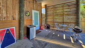 Eine Terrasseneinrichtung im Freien mit Holzzaun, Grill, Tisch mit Stühlen und Mülleimer.