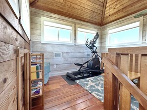 A wooden interior with a stationary bike, a bookshelf, and a window. - The Lookout: North Cape, 3 Bedrooms, Pet-Friendly, Private Pool! Short walk to b (Cape San Blas)