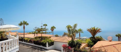 A coastal residential area with a clear view of the sea, a white fence, and a satellite dish on a building.