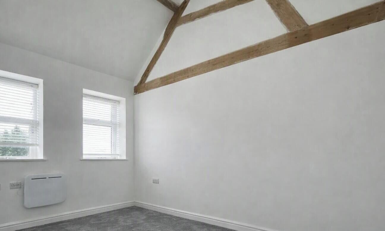 A room with two windows, a white radiator, and exposed wooden beams on the ceiling.