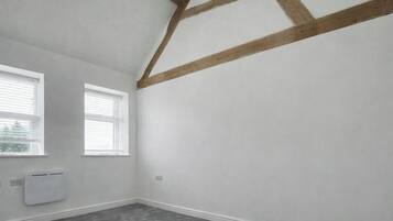 A room with two windows, a white radiator, and exposed wooden beams on the ceiling.